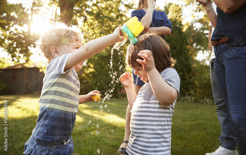 Child pouring water over his riends head in the garden  photo