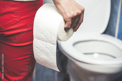 Woman suffers from diarrhea holds toilet paper roll in front of toilet bowl. Stomach upset. photo