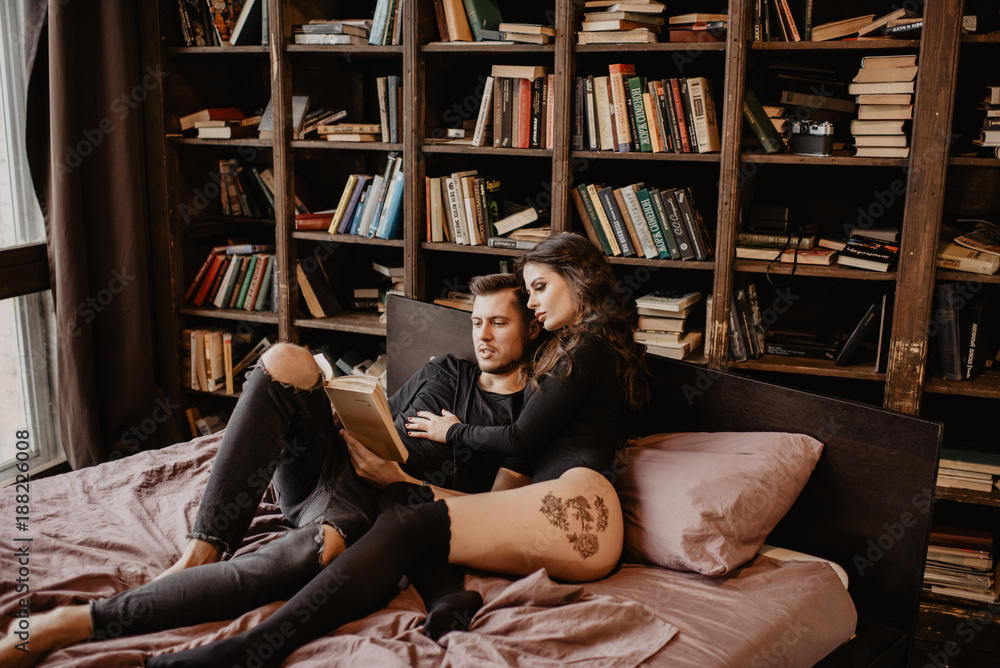 Young smiling couple reading book sitting on bed in bedroom Young smiling couple reading book sitting on bed in bedroom