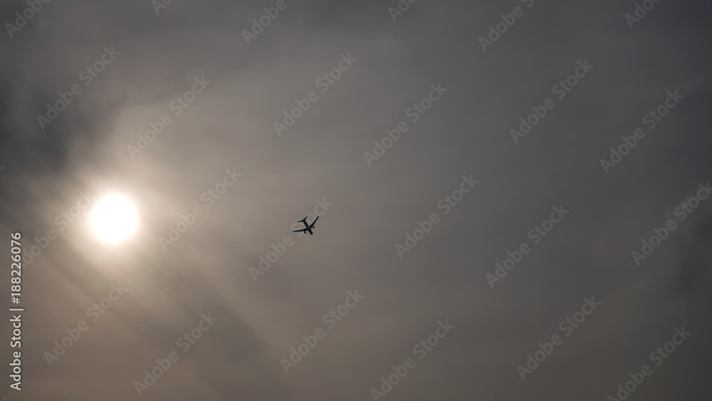 The Sun and Silhouette of an Airplane Flying in Cloudy Sky The Sun and Silhouette of an Airplane Flying in Cloudy Sky