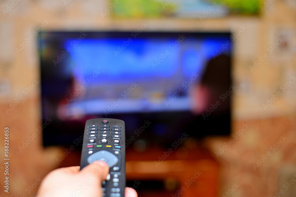 The man with the remote control in hand watching the sports channel and presses the button on the remote control. Remote control in hand closeup. The man with the remote control in hand watching the sports channel and presses the button on the remote control. Remote control in hand closeup.