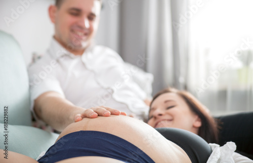 Young happy pregnant couple relaxing on sofa at home  touching belly