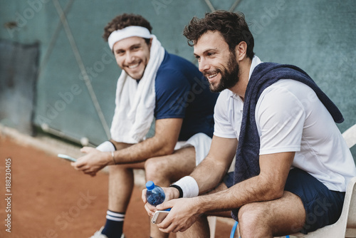 Two young men having a break after a tennis match on a clay court