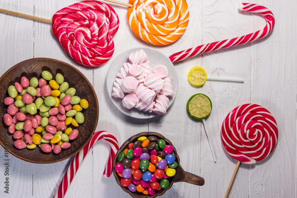Colorful chocolate candies, lollipops, candy cane and marshmallows on wooden table Colorful chocolate candies, lollipops, candy cane and marshmallows on wooden table