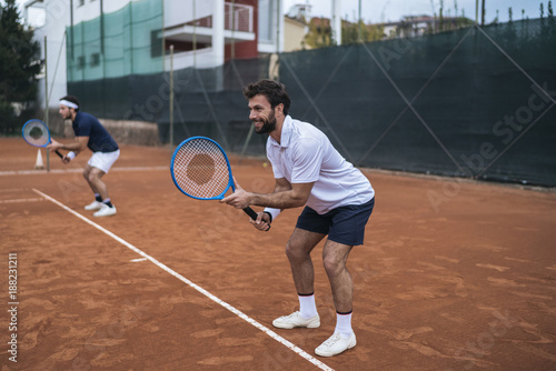 Group of friends play tennis a double match on a clay court