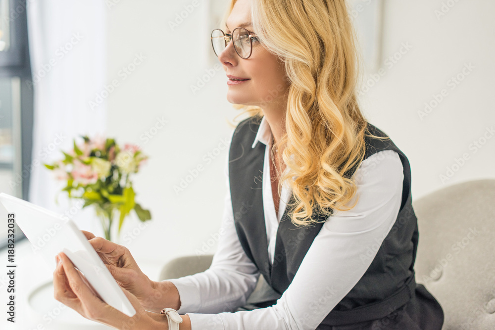 pensive middle aged businesswoman in eyeglasses using digital tablet and looking away pensive middle aged businesswoman in eyeglasses using digital tablet and looking away
