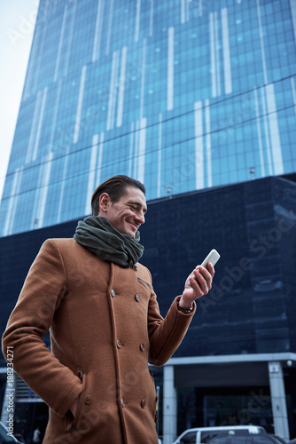 side view beaming man sending message by phone while walking on street. Gadget concept