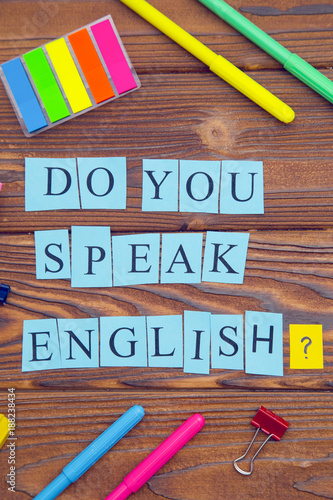 Learning Foreign Languages concept: Do you speak English inscription on blue paper and bright colorful office supplies on a rustic wooden background, top view