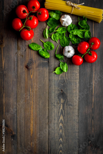 Main ingredients for italian pasta. Spaghetti  tomatoes  garlic  green basil on dark wooden background top view copy space
