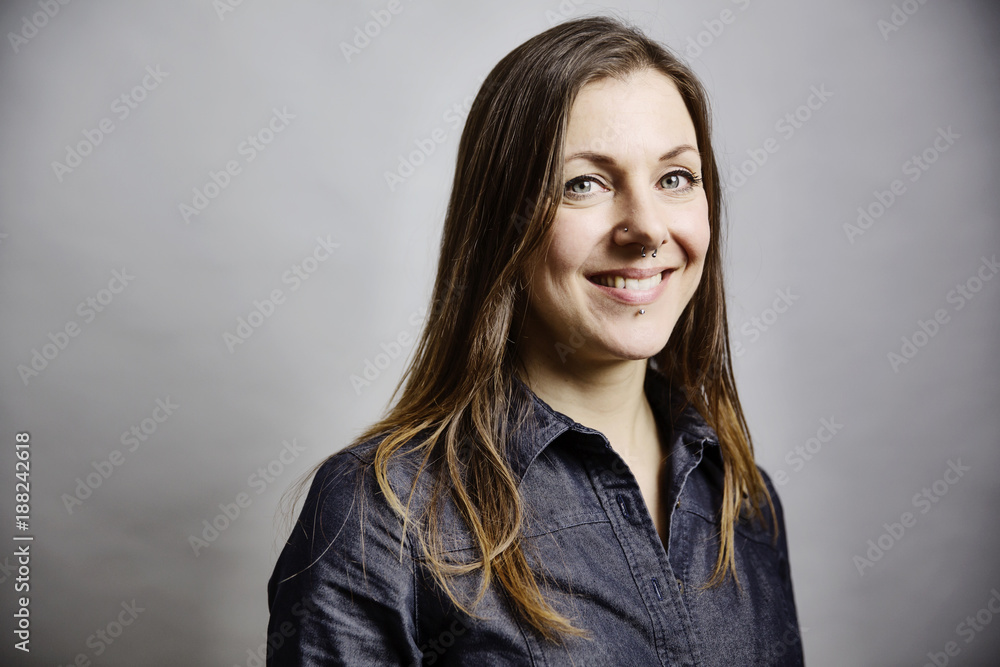 junge Frau mit langem Haar und Piercings im Gesicht, Portrait vor grauem Hintergrund junge Frau mit langem Haar und Piercings im Gesicht, Portrait vor grauem Hintergrund