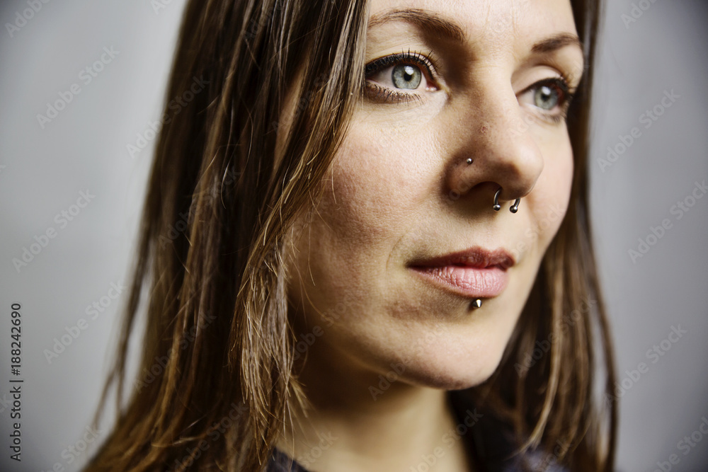 junge Frau mit langem Haar und Piercings im Gesicht, Portrait vor grauem Hintergrund StockFoto