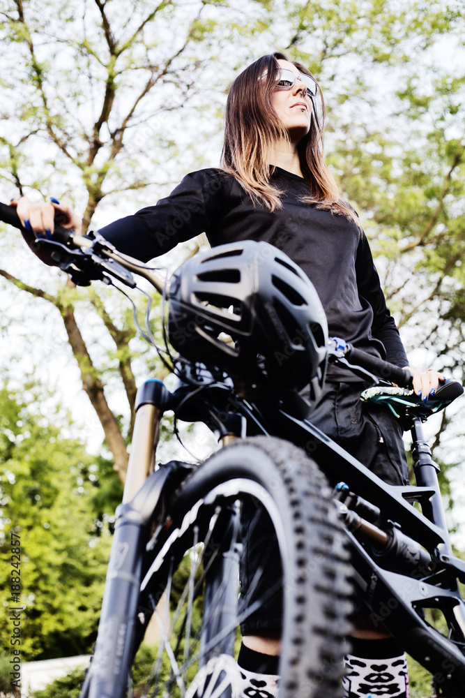 Fototapeta premium junge Bikerin mit Sonnenbrillesteht neben ihrem Mountainbike,Köln, Nordrhein-Westfalen, Deutschland