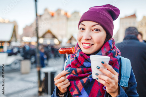 Canvas Print young woman traveler snacks a sausage with a hot drink on the street of a Europe