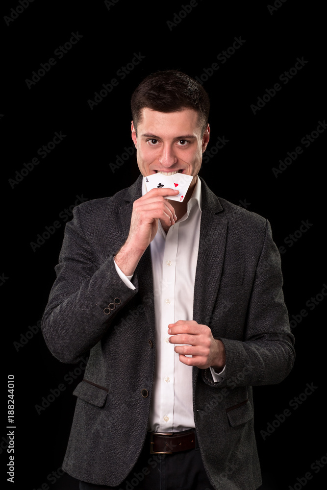 Young caucasian man wearing suit holding two aces in his hand and teeth on black background. Gambling concept. Casino Young caucasian man wearing suit holding two aces in his hand and teeth on black background. Gambling concept. Casino