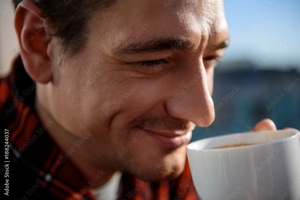 Close up portrait of happy adult man drinking coffee outside in the morning. He is holding a cup in hand with calm look. Focus on his face Close up portrait of happy adult man drinking coffee outside in the morning. He is holding a cup in hand with calm look. Focus on his face
