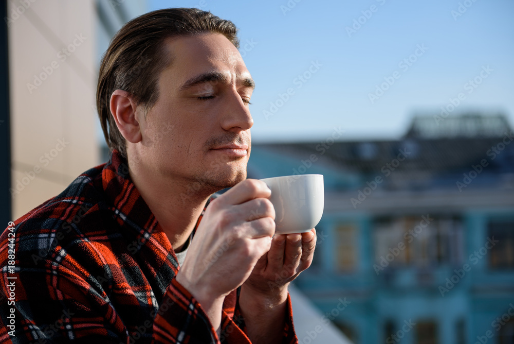 How it smells. Portrait of calm guy standing outside and holding a cup, he is smelling drink with closed eyes. Copy space in right side How it smells. Portrait of calm guy standing outside and holding a cup, he is smelling drink with closed eyes. Copy space in right side