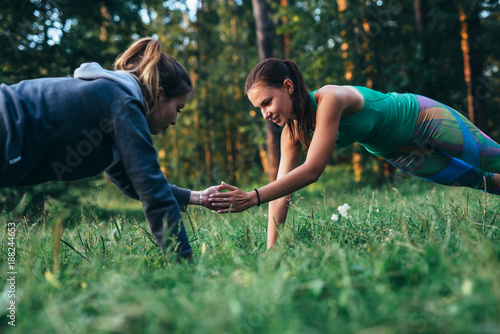 Two girls doing buddy workout outdoors performing push-ups to clap on grass © undrey