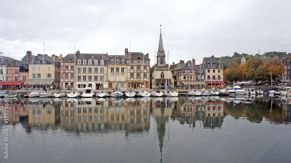 Obraz premium HONFLEUR, FRANCE - Scenic view of church and saling boats in old medieval harbor, beautiful buildings in historic city center, people are relaxing at terraces along the harbour in old town