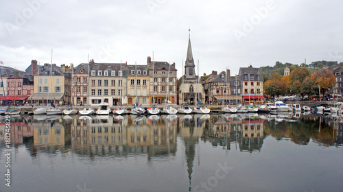 HONFLEUR, FRANCE - Scenic view of church and saling boats in old medieval harbor, beautiful buildings in historic city center, people are relaxing at terraces along the harbour in old town