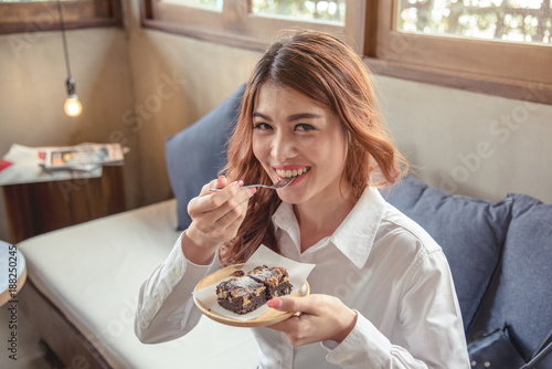 Portrait beautiful young adult woman look cheerful relaxing with dessert while sitting on furniture.
