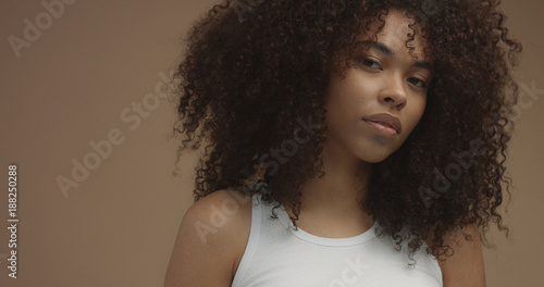 mixed race black woman portrait with big afro hair, curly hair in beige background