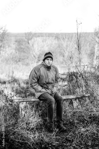 A young man sits on an old bench in the countryside in the autumn time.
