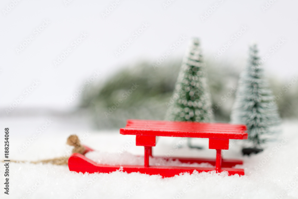 roter Spielzeugschlitten im Schnee vor Tannen