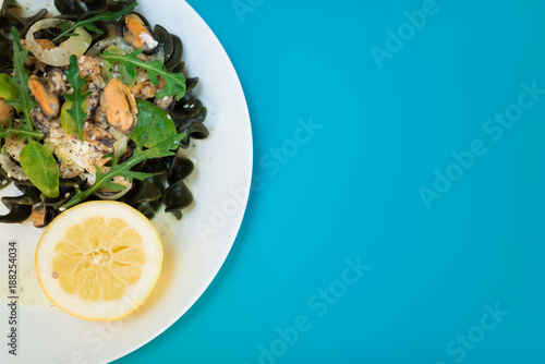 Black pasta with seafood in white cream sauce and lemon. Blue background