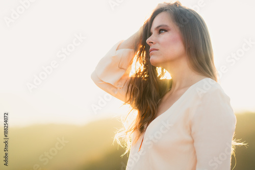 Close up of young mixed race woman in white dress standing above a valley at sunrise