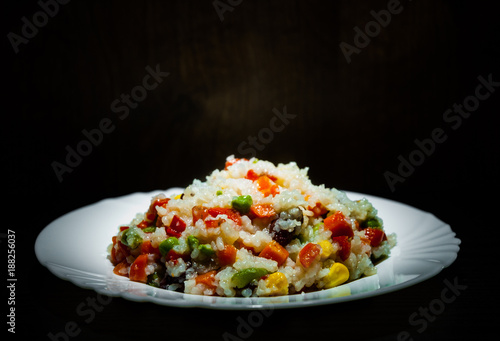 Rice with mixed vegetables on white plate  
 on dark wooden background with copy space.
