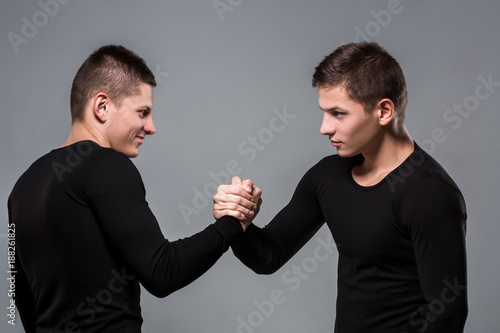 Portrait of young twin brothers standing face to face on gray ba