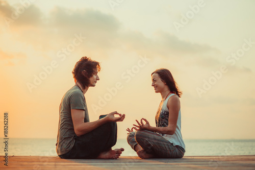 Young couple is doing yoga on the sunrise background.
