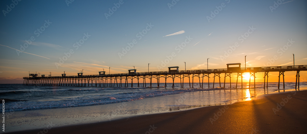 Colorful Sunset at ocean coast with silhouette of pier and photographer