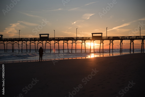 Colorful Sunset at ocean coast with silhouette of pier and photographer