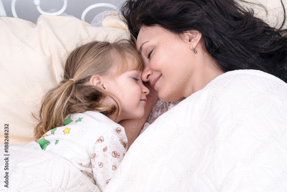 Mom and little daughter are lying in bed with their eyes closed nose to nose Mom and little daughter are lying in bed with their eyes closed nose to nose