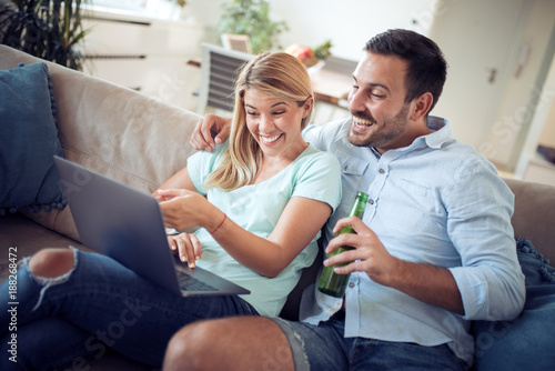 Couple sitting on sofa and using laptop at home.