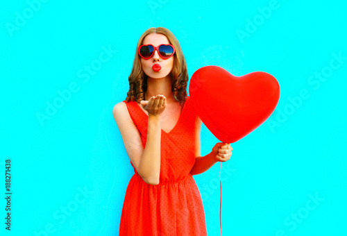 Portrait pretty woman sends an air kiss with red air balloons on blue background