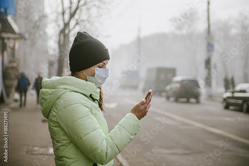 woman stands near a road in the city in a protective medical mask. Protection from viruses in the city.