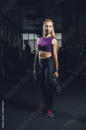 Close-up portrait of muscular young girl training with barbells in the gym. Brutal athletic girl with a six-pack, perfect abs, shoulders, biceps, triceps and chest 