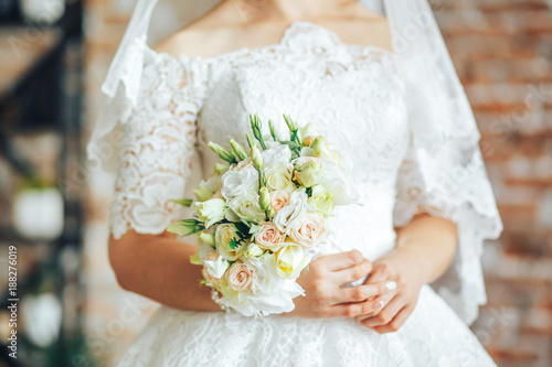 Beautiful light wedding bouquet with white roses in the hands of the bride