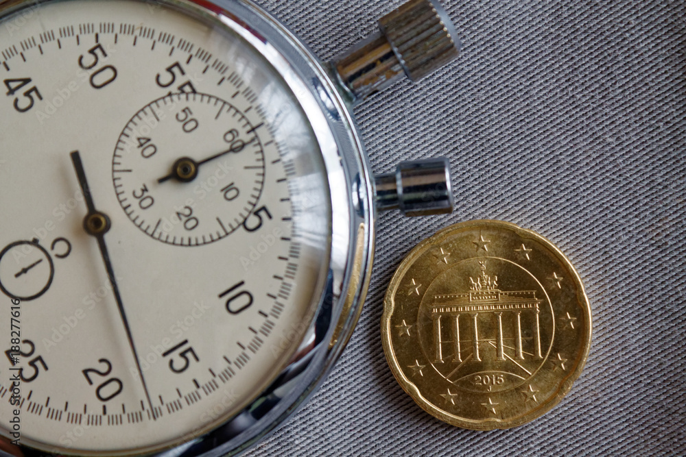 Euro coin with a denomination of twenty euro cents (back side)and stopwatch on gray denim backdrop - business background