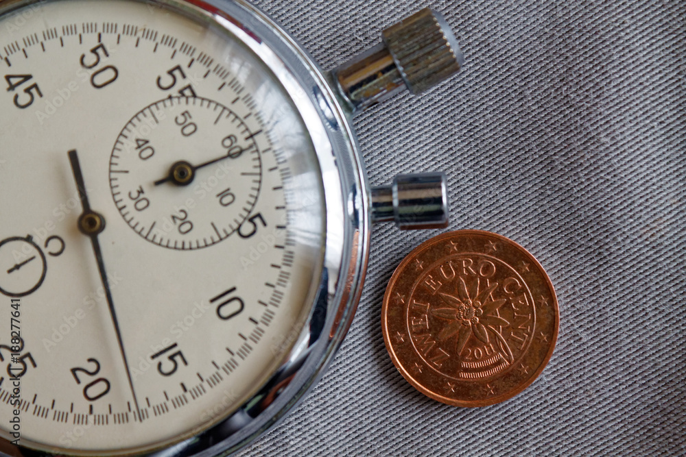 Euro coin with a denomination of two euro cents (back side) and stopwatch on gray denim backdrop - business background Euro coin with a denomination of two euro cents (back side) and stopwatch on gray denim backdrop - business background