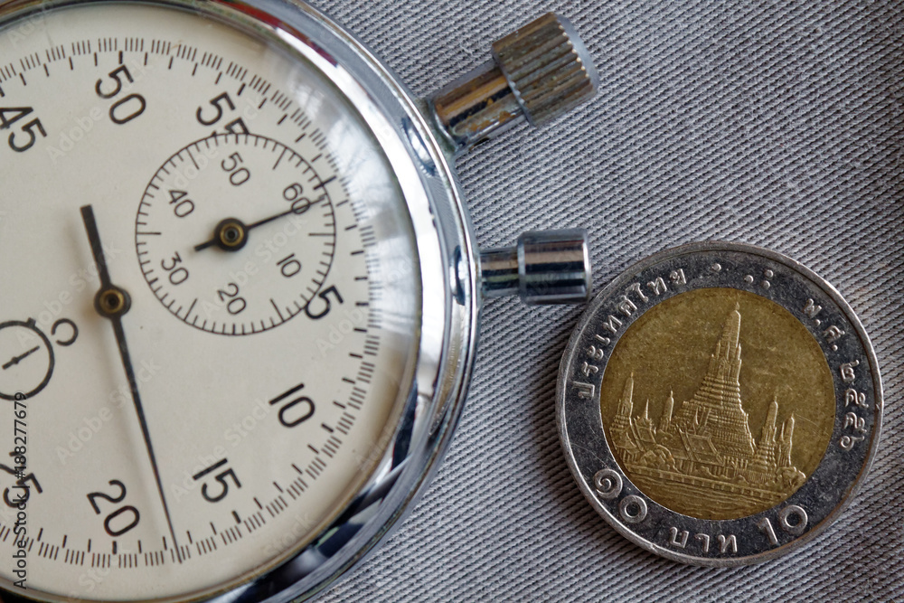 Thai coin with a denomination of 10 baht and stopwatch on gray denim backdrop - business background