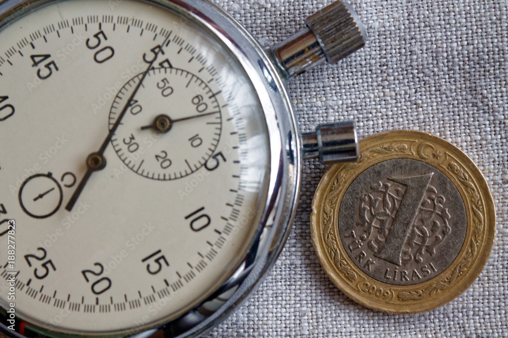 Turkish coin with a denomination of 1 lira and stopwatch on gray linen backdrop - business background Turkish coin with a denomination of 1 lira and stopwatch on gray linen backdrop - business background