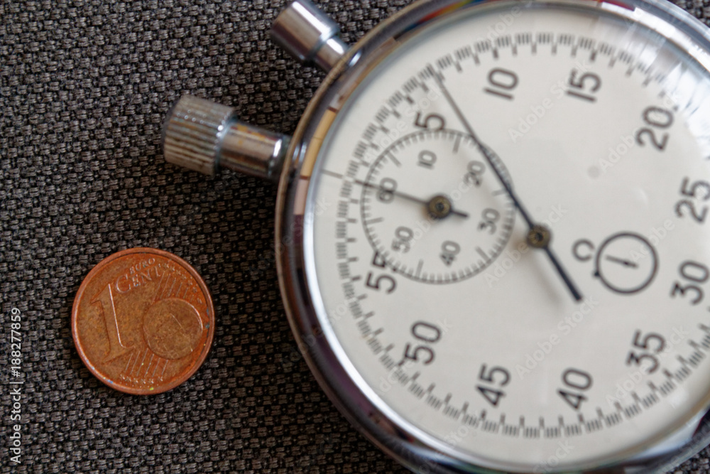 Euro coin with a denomination of 1 euro cent and stopwatch on brown denim backdrop - business background Euro coin with a denomination of 1 euro cent and stopwatch on brown denim backdrop - business background