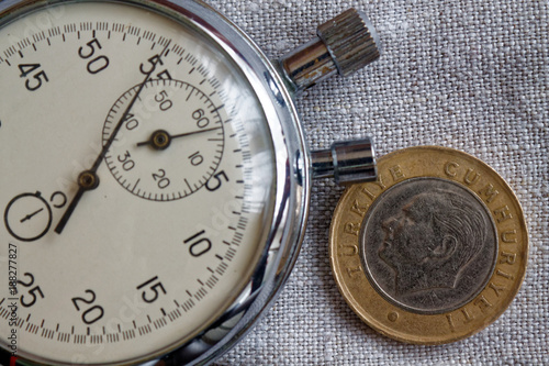 Turkish coin with a denomination of one lira (back side) and stopwatch on gray flax backdrop - business background