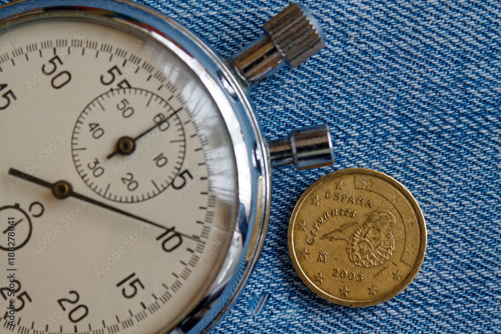 Euro coin with a denomination of ten euro cents (back side) and stopwatch on blue denim backdrop - business background