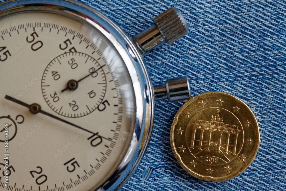 Euro coin with a denomination of twenty euro cents (back side) and stopwatch on blue denim backdrop - business background