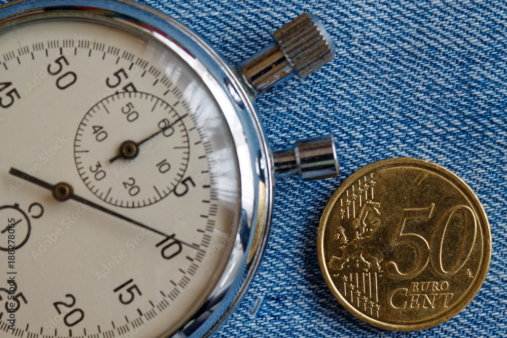 Euro coin with a denomination of 50 euro cents and stopwatch on blue denim backdrop - business background