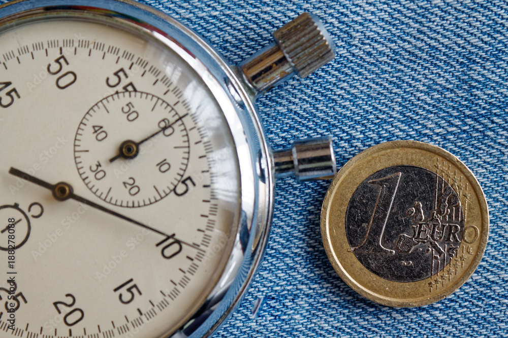 Euro coin with a denomination of 1 euro and stopwatch on blue denim backdrop - business background